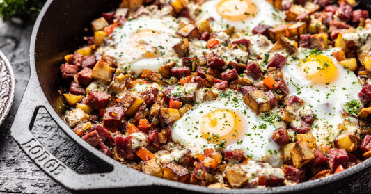 A cast iron skillet with four eggs resting atop the corned beef hash, ready to be served
