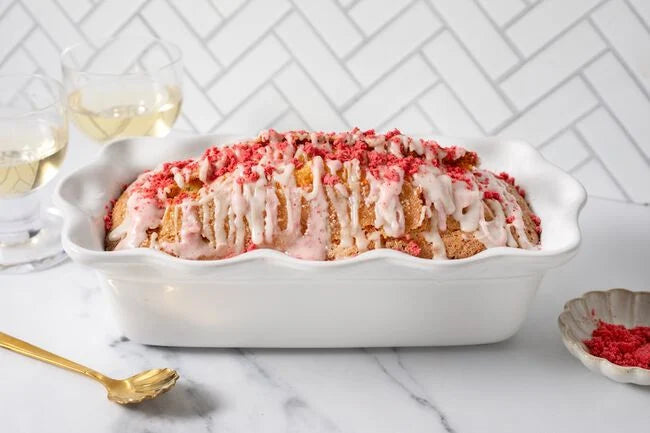 A loaf cake in a white Le Creuset loaf dish, topped with strawberry drizzle and freeze dried strawberries.