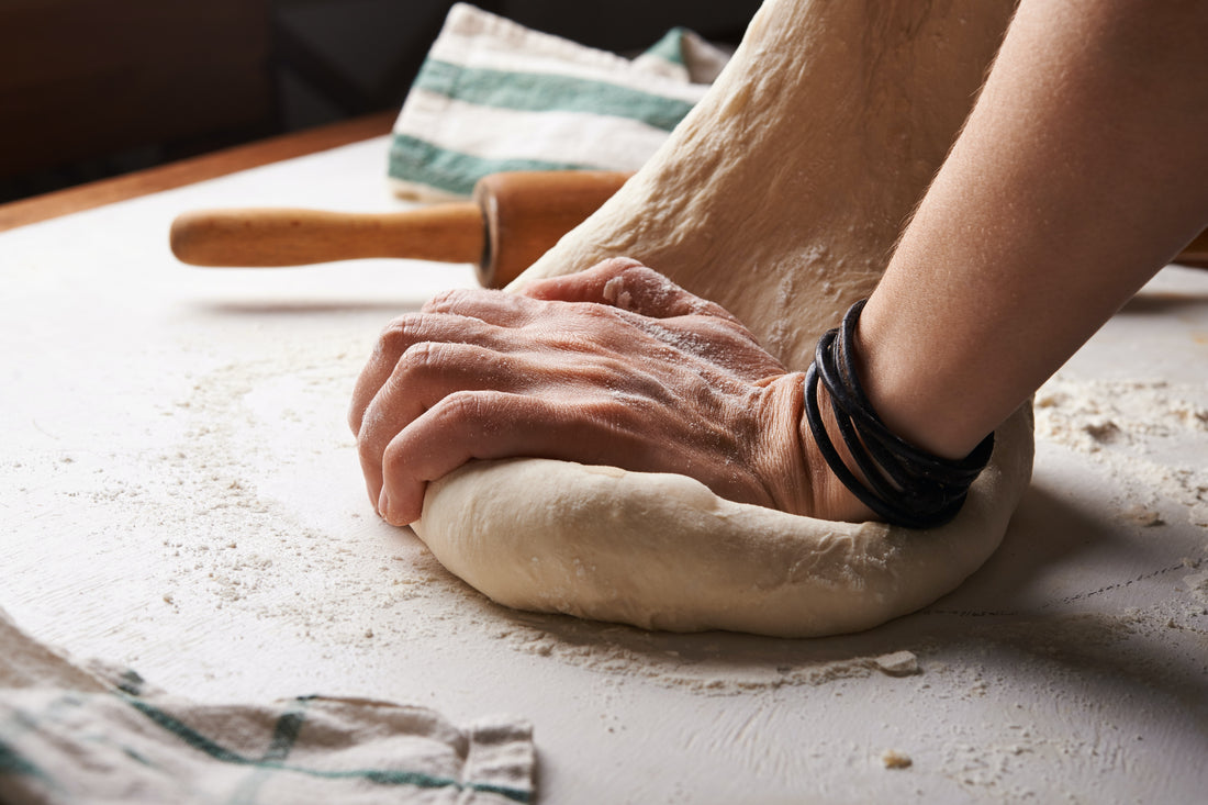Hands kneading a ball of pizza dough.
