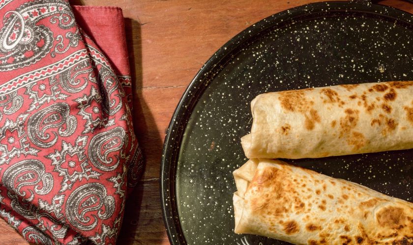 Two grilled burritos on a black speckled plate next to a western style bandana. 