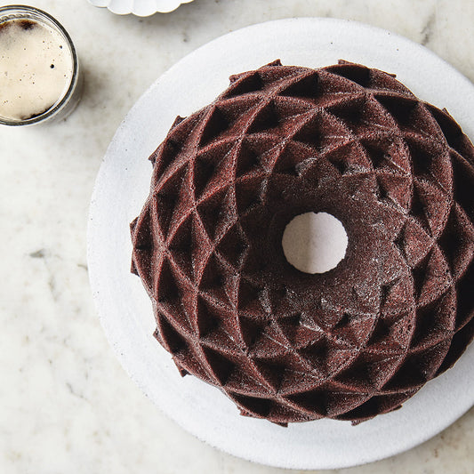 A chocolate bundt cake sitting on a white plate next to a jar of frosting